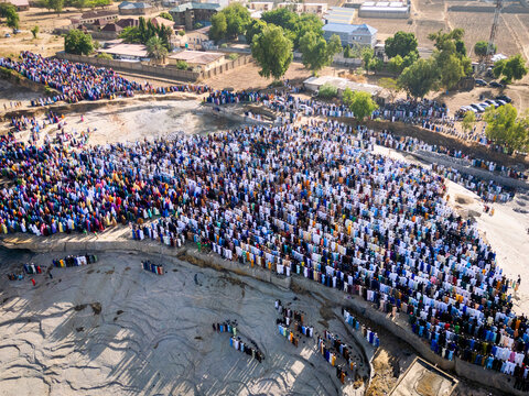 Zaria, Nigeria - 28 October 2025: Aerial view of a large crowd of people gathered for prayer at the Jum'at Mosque, Hayin Dogo Palladan, on a rocky landscape under bright sunlight.