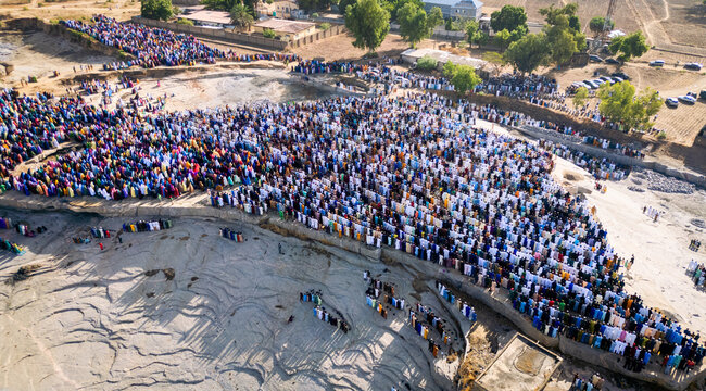 Zaria, Nigeria - 28 October 2025: Aerial view of a large crowd of people gathered for prayer at the Jum'at Mosque, Hayin Dogo Palladan, on a rocky landscape under bright sunlight.