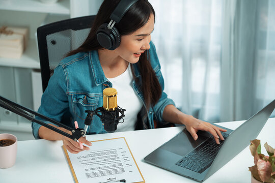 Host channel Asian influencer talking in broadcast streaming online wearing headset on social media live with script note, greeting listeners in life coaching or marketing at modern studio. Stratagem.