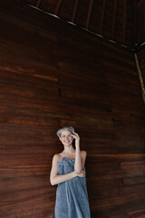 Fototapeta premium smiling woman wrapped in towel with hair wrap standing against wooden wall, relaxed and fresh indoors, wellness and spa concept