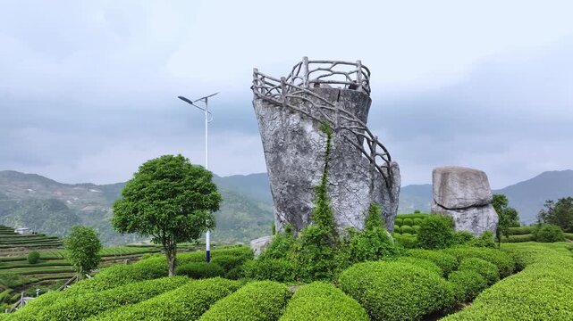 Stone sculpture viewing platform on mountain top surrounded by tea plantations and distant mountains