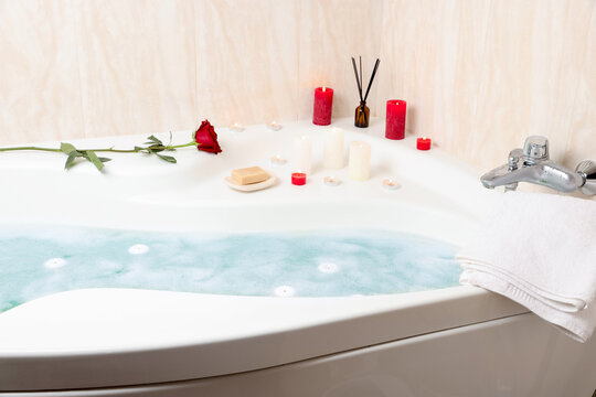 Romantic atmosphere. Bathtub with burning candles, towels, air reed freshener, red rose and soap in bathroom, closeup