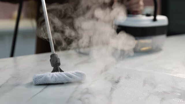 Woman cleaning white marble countertop with steam cleaner at home, closeup. Camera moving backwards