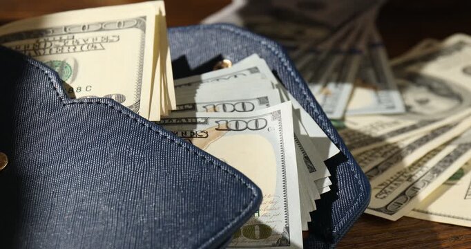 Woman counting money at wooden table, focus on wallet with old and new hundred dollar bills