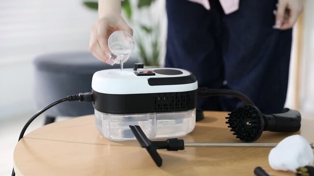 Woman pouring water into steam cleaner at wooden table indoors, closeup. Camera moving left