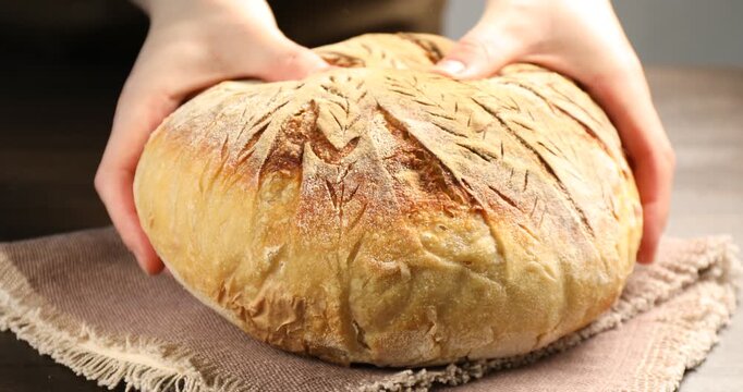 Woman with loaf of freshly baked sourdough bread at wooden table, closeup