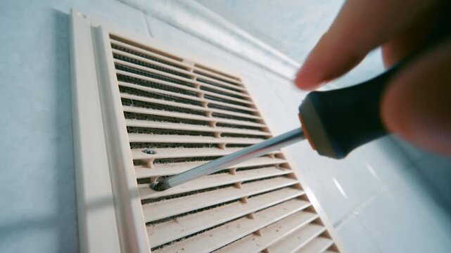 Hand with Screwdriver Removing Screws from Dusty Ventilation Grille | HVAC Vent Cover Disassembly for Cleaning and Maintenance | Home Repair and Air System Service. Close-Up Wide-Angle View