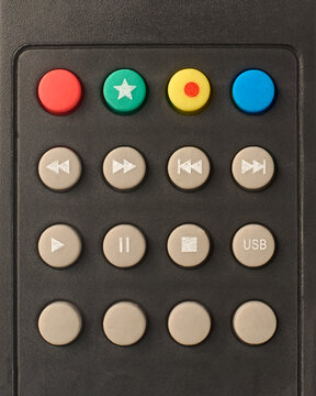 media playback and function buttons on matte black plastic remote control, red green yellow blue and grey rubber buttons with white symbols, top view closeup in full frame background