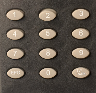 numeric keypad on matte black plastic remote control, oval grey rubber buttons with white numbers and labels, top view closeup in full frame background