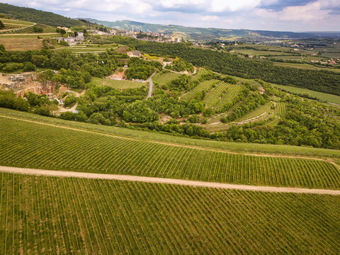 Aerial view of Pieve di San Giorgio and lush vineyards on rolling hills with stone walls and a dirt path in San Giorgio di Valpolicella, Veneto, Italy.