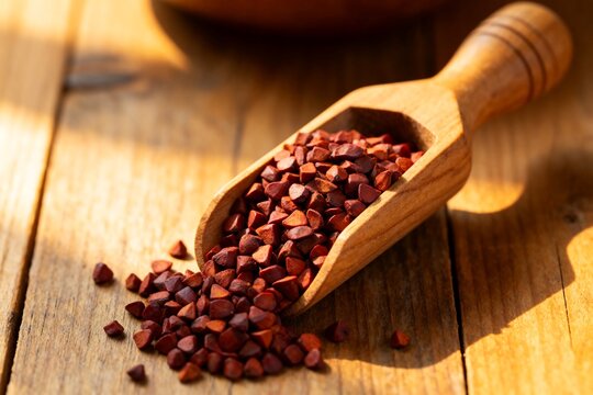 Wooden scoop filled with Annatto seeds on rustic table, warm sunlight