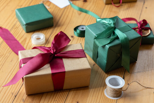 Brown kraft gift with burgundy ribbon sitting on wooden tabletop with two green gifts, twine, tape