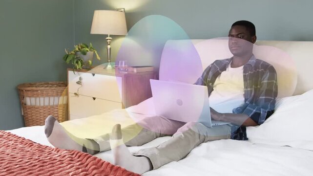 Man on bed using laptop for technology, glancing, typing while color overlay drifting across frame