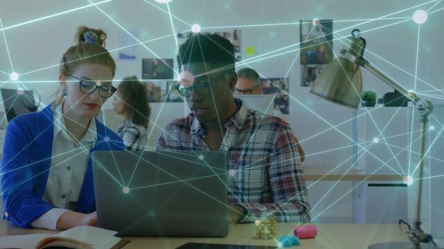 Woman leaning pointing to biz laptop and book, man typing as network overlay drifting across faces