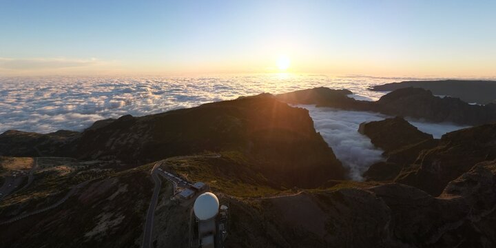 Aerial view of the Pico do Arieiro radar station on a rugged mountain peak above a thick sea of clouds at sunset Madeira, Portugal.