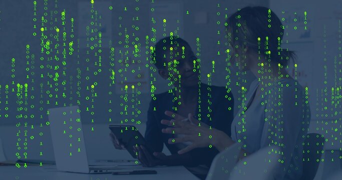 Discussing data, two coworkers in workwear viewing tablet in office with laptop, binary overlay