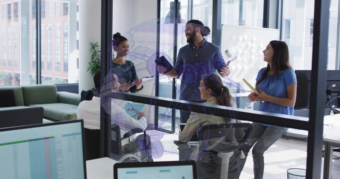 Presenting team lead wearing dark shirt holding tablet and pointing in glass room with monitors
