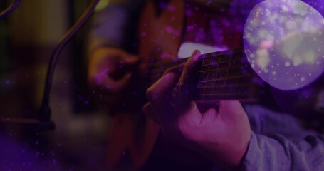 Fototapeta premium Playing guitarist fretting and strumming guitar in dim studio in longsleeve shirt with mic, bokeh