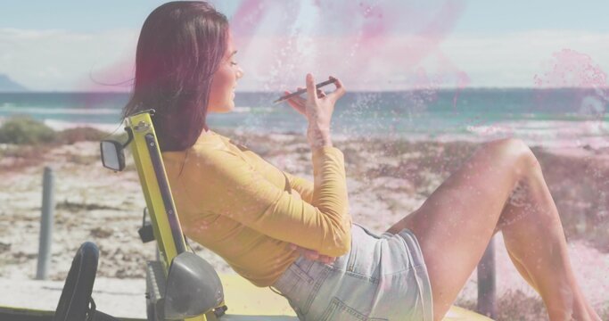 Reclining woman wearing mustard-top denim-shorts leaning on yellow dune buggy at beach, holding pen