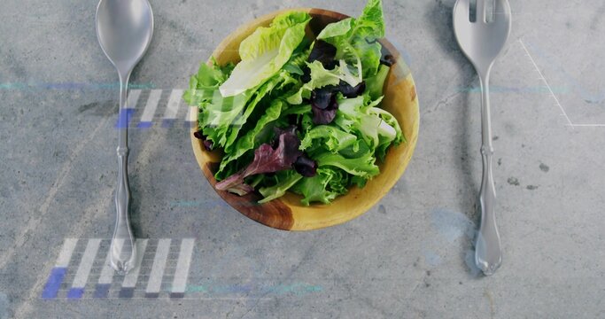 Displaying wooden salad bowl holding green-and-purple leaves on gray tabletop spoon left fork right