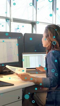Vertical video: Analyst using pad comparing business data to print charts, blue circles across desk
