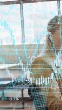 Vertical video: Pan showing woman in chair turning as finance charts animating to monitor market