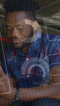 Vertical video: Man seated looking at phone, tapping and swiping to review tech data as HUD grows