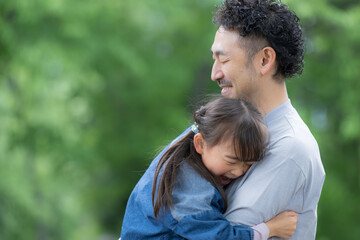 Fototapeta premium 新緑の公園で父親に抱きつく笑顔の女の子 親子愛と幸せな家族時間 父の日などのイメージにも