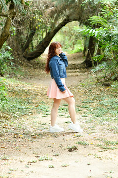 Chica latina bonita en medio de una camino rodeado de arboles y naturaleza verde al aire libre. Mujer bonita con chaqueta azul y vestido rosado.