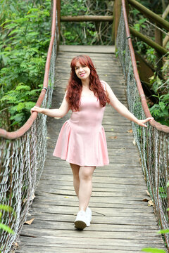 Mujer joven latina de pie sobre un puente colgante de madera, usando un vestido rosado, cabello largo y casta&ntilde;o. Bonito cuerpo.