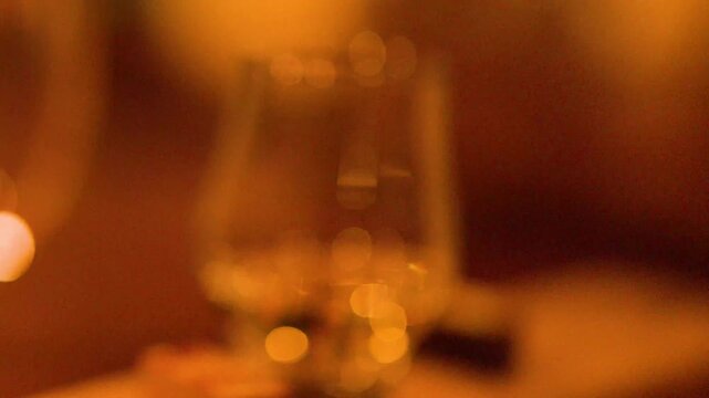 Cinematic close up of scotch whiskey being swirled in traditional glass with warm atmospheric lighting and bokeh.