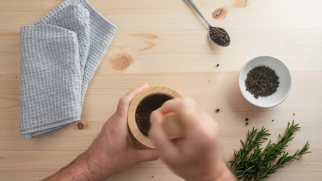 Man grinding black peppercorns with wooden mortar and pestle
