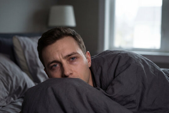 Tired young man suffering from insomnia lying awake in bed