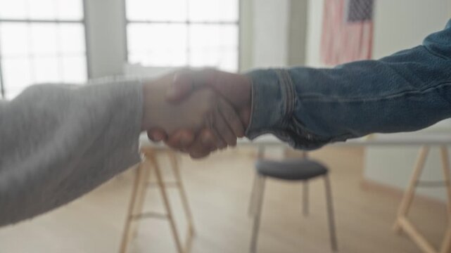 Man and woman shake hands firmly beside a vote sign and us flag inside a public building; civic duty solidarity.
