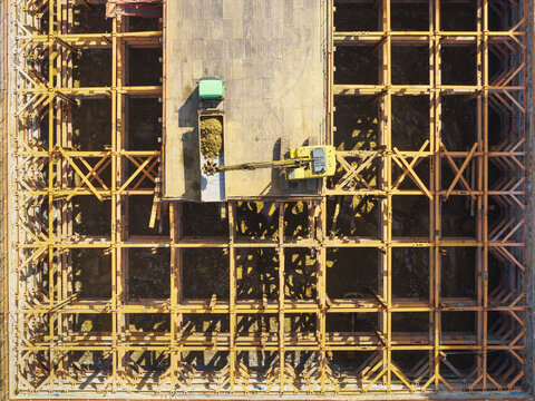 Aerial view of building foundation engineering with a yellow excavator and a green truck on a steel grid structure in Taiwan.