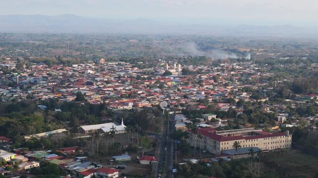 Diriamba city skyline shows a mix of houses and buildings set in green landscape. Smoke rises in the distance. This is a daytime view taken from above.