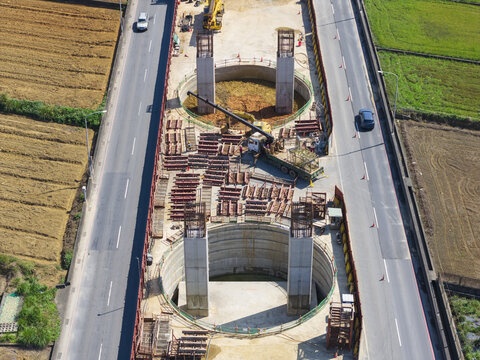 Aerial view of elevated highway construction site featuring concrete pillars, deep circular foundations, and heavy machinery between existing roads and green fields in Taiwan.