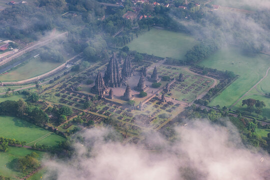 Aerial view of the ancient Prambanan Temple complex with its towering stone spires surrounded by lush green grounds and morning mist in Kecamatan Prambanan, Daerah Istimewa Yogyakarta, Indonesia.