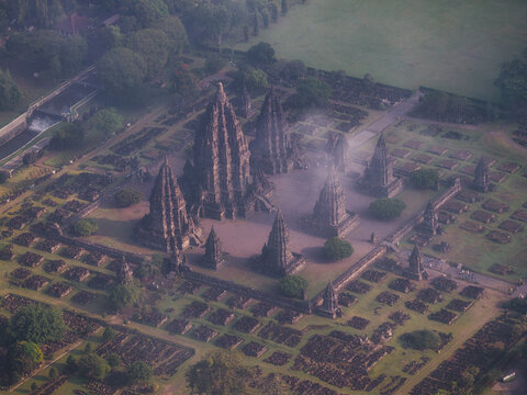 Aerial view of Prambanan Temple with its ancient stone spires, surrounding ruins, and lush green grounds under a soft morning mist Kecamatan Prambanan, Daerah Istimewa Yogya, Indonesia.