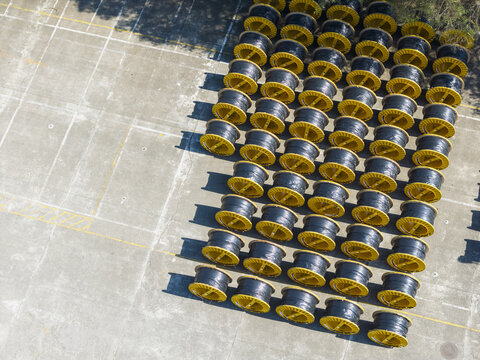 Aerial view of rows of industrial cable reels with yellow rims and black cables neatly arranged on a concrete storage yard in Taiwan.