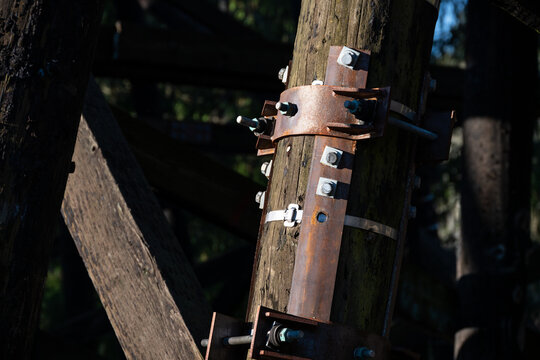 Closeup of galvanized iron pole splint, reinforcing metal with collar clamps on old wooden train trestle structural support beams, repair detail
