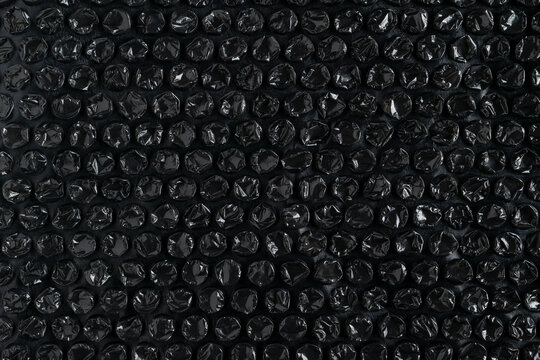 Top view of black bubble wrap texture background. High-contrast plastic packaging material with glossy air-filled bubbles for shipping and fragile item protection.