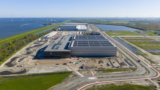 Aerial view of the JYSK DCL construction site featuring a large warehouse with solar panels near a coastal wind farm in Lelystad, Flevoland, Netherlands.
