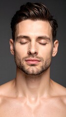 Fototapeta premium Portrait of a man with closed eyes against a plain gray background. His skin is fair, and he has a short, trimmed beard and neatly styled hair