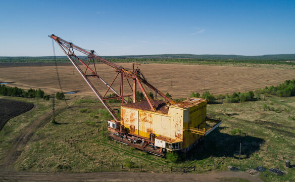 Massive industrial dragline excavator rests in an open field, surrounded by sparse vegetation and dirt roads