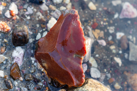 Ancient red chert scraper, a stone age tool discovered on a river bank, showcasing weathered textures and the allure of prehistoric finds