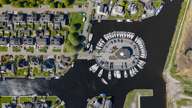 Aerial view of Enjoy Sailing Zeiljachtverhuur marina with sailboats docked in a circular pattern and nearby residential houses in Lemmer, Friesland, Netherlands.