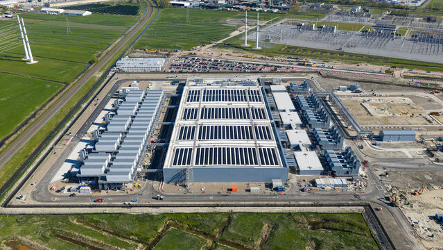 Aerial view of Datacenter Westpoort featuring extensive solar panels on the roof and cooling systems surrounded by green fields in Groningen, Groningen, Netherlands.
