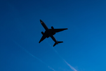 Fototapeta premium Airplane silhouette flying in blue sky. Jet aircraft during flight. Airliner moving through clear sky. Airplane in motion. Aviation concept with flying jet against sky. Passenger aircraft takeoff.