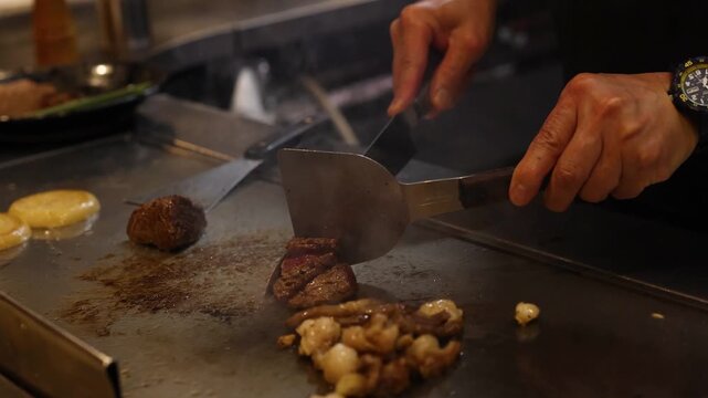 Professional chef cutting premium beef steak on hot iron teppanyaki grill in traditional japanese restaurant.